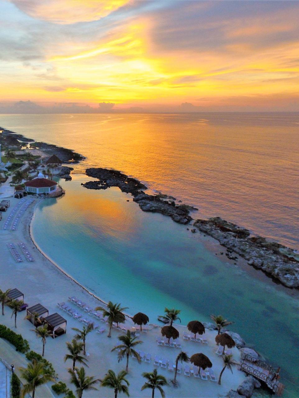 Wide aerial view of a Caribbean coastal resort showing reef structures, swimming pools, and beachfront